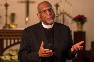 Fr. Masud preaches in a church while wearing a clerical collar.
